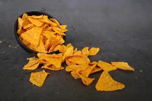 Tortilla-Chip ist Maischips oder nennt sich Nachos, serviert in einer Schüssel, auf schwarzem Hintergrund aus Mais foto