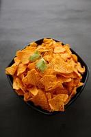 Tortilla-Chip ist Maischips oder nennt sich Nachos, serviert in einer Schüssel, auf schwarzem Hintergrund aus Mais foto