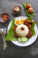 Nasi Lemak ist ein traditionelles malaiisches Gericht aus gekochten Eiern, Bohnen, Sardellen, Chilisauce und Gurken. aus einem Gericht, das auf einem Bananenblatt serviert wird foto