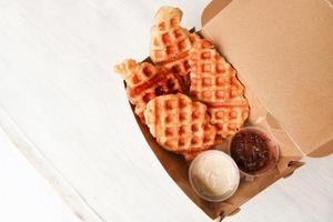 Croissant-Waffel oder Croffle mit Schokoladensauce, serviert in Schachtel und weißem Hintergrund foto