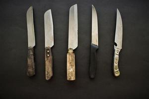 Viele Messer liegen zum Kochen auf schwarzem Hintergrund foto