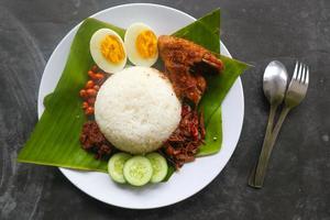 Nasi Lemak ist ein traditionelles malaiisches Gericht aus gekochten Eiern, Bohnen, Sardellen, Chilisauce und Gurken. aus einem Gericht, das auf einem Bananenblatt serviert wird foto