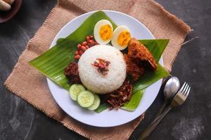 Nasi Lemak ist ein traditionelles malaiisches Gericht aus gekochten Eiern, Bohnen, Sardellen, Chilisauce und Gurken. aus einem Gericht, das auf einem Bananenblatt serviert wird foto
