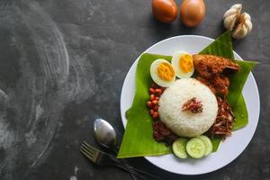 Nasi Lemak ist ein traditionelles malaiisches Gericht aus gekochten Eiern, Bohnen, Sardellen, Chilisauce und Gurken. aus einem Gericht, das auf einem Bananenblatt serviert wird foto