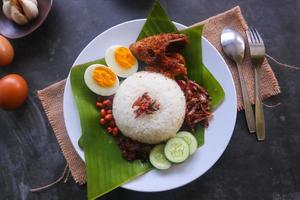 Nasi Lemak ist ein traditionelles malaiisches Gericht aus gekochten Eiern, Bohnen, Sardellen, Chilisauce und Gurken. aus einem Gericht, das auf einem Bananenblatt serviert wird foto