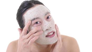 Schönheitsverfahren und Hautpflege. Nahaufnahme Porträt eines glücklich lachenden, oben ohne asiatischen Mannes mit Gesichtsmaske, die sein Gesicht berührt. isoliert auf weißem Hintergrund. foto