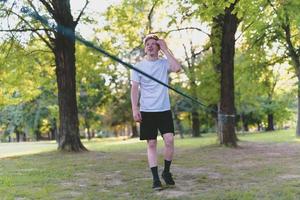 junger Mann balanciert und springt auf Slackline. Mann geht, springt und balanciert auf einem Seil im Park. foto