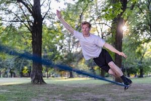 junger Mann balanciert und springt auf Slackline. Mann geht, springt und balanciert auf einem Seil im Park. foto