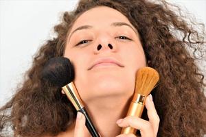 schöne junge lächelnde frau tragen make-up mit pinsel auf. isoliert foto