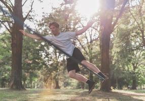 junger Mann balanciert und springt auf Slackline. Mann geht, springt und balanciert auf einem Seil im Park. foto