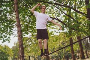 junger Mann balanciert und springt auf Slackline. Mann geht, springt und balanciert auf einem Seil im Park. foto