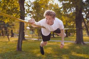 junger Mann balanciert und springt auf Slackline. Mann geht, springt und balanciert auf einem Seil im Park. foto