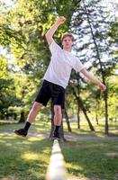 junger Mann balanciert und springt auf Slackline. Mann geht, springt und balanciert auf einem Seil im Park. foto