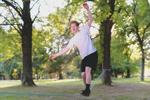 junger Mann balanciert und springt auf Slackline. Mann geht, springt und balanciert auf einem Seil im Park. foto