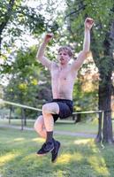 junger Mann balanciert und springt auf Slackline. Mann geht, springt und balanciert auf einem Seil im Park. foto