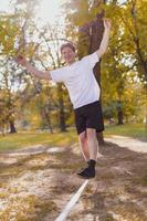 junger Mann balanciert und springt auf Slackline. Mann geht, springt und balanciert auf einem Seil im Park. foto