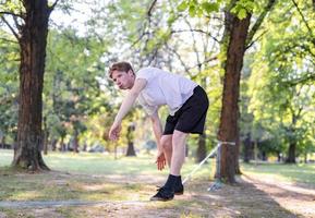 junger Mann balanciert und springt auf Slackline. Mann geht, springt und balanciert auf einem Seil im Park. foto