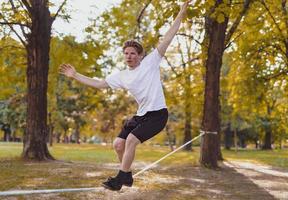 junger Mann balanciert und springt auf Slackline. Mann geht, springt und balanciert auf einem Seil im Park. foto