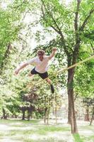 junger Mann balanciert und springt auf Slackline. Mann geht, springt und balanciert auf einem Seil im Park. foto