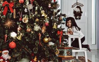 asiatische kleine Mädchen schmücken den Weihnachtsbaum drinnen. am morgen vor weihnachten. Porträt liebendes Mädchen aus nächster Nähe. foto