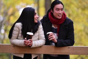 Gemischtes Paar im Park, das sich amüsiert und Kaffee trinkt foto