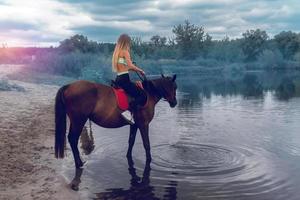 Schlankes Mädchen zu Pferd in der Nähe des Sees foto