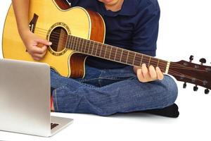 Konzentrieren Sie sich auf die Hände des Kindes oder Teenagers, das Akustikgitarre und einen Laptop im Vordergrund auf weißem Hintergrund spielt. Lern- und Entspannungskonzept. foto