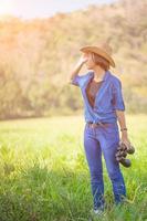 Frau trägt Hut und hält Fernglas auf der Wiese foto