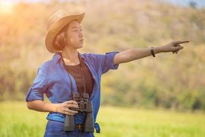 Frau trägt Hut und hält Fernglas auf der Wiese foto