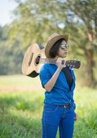 Frau trägt Hut und trägt ihre Gitarre auf der Wiese foto