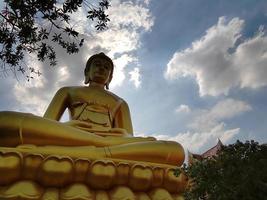goldene große buddha-statue phra buddha dhammakaya thep mongkol im wat pak nam phasi charoen tempel. sonnenlicht, himmel und wolkenhintergrund foto