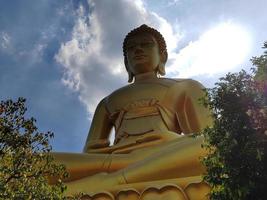 goldene große buddha-statue phra buddha dhammakaya thep mongkol im wat pak nam phasi charoen tempel. sonnenlicht, himmel und wolkenhintergrund foto