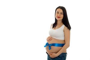 schöne junge brünette schwangere Mädchen mit blauem Klebeband auf ihrem Bauch posiert isoliert auf weißem Hintergrund foto