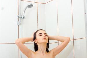 junges schönes mädchen steht unter der dusche, schließt ihre augen und wäscht hände haare foto