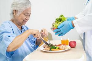 asiatische senior oder ältere alte damenpatientin, die frühstück und gemüse gesundes essen mit hoffnung und glücklich isst, während sie im krankenhaus sitzt und hungrig auf dem bett sitzt. foto