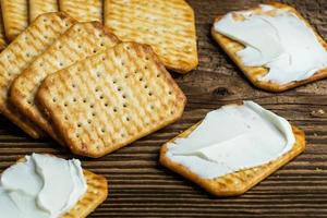 mit Käse bestrichene Cracker als leichter Snack auf einem Holzbrett foto