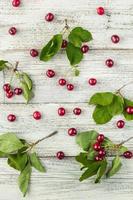 Rote reife Kirschbeeren und grüne Blätter auf weißem Holzhintergrund. Ansicht von oben foto