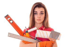 überraschtes junges brünettes Baumeistermädchen in Uniform macht Renovierung mit Werkzeugen in ihren Händen isoliert auf weißem Hintergrund foto