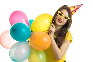 lächelndes junges Mädchen mit Brille und auf dem Kopfkegel hält viele farbige Ballons foto