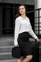 schöne schlanke Geschäftsfrau in einem weißen Hemd und einem Rock, der eine Tasche hält foto
