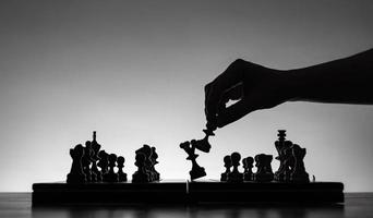 Schachbrett mit Schachfiguren Silhouetten auf weißem Hintergrund. konzept von geschäftsideen und wettbewerbs- und strategieideen. klassisches Kunstfoto in Schwarz-Weiß. die Königin schlagen.