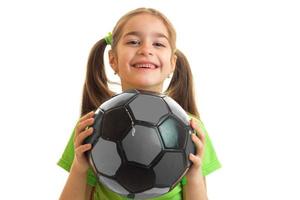 Kleines fröhliches Mädchen in grüner Uniform, das mit Fußball spielt foto