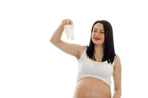 schöne junge brünette schwangere Mädchen mit kleinen weißen Socken in ihren Händen posiert isoliert auf weißem Hintergrund foto