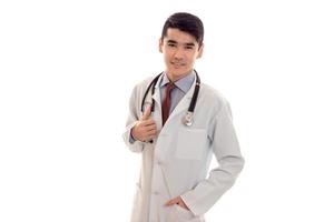 hübscher junger männlicher Arzt in Uniform mit Stathoskop, der die Kamera anschaut und isoliert auf weißem Hintergrund lächelt foto
