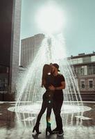 Fröhliches junges Paar umarmt sich am Straßenbrunnen foto