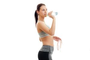 junges fitnessmädchen steht seitlich und trinkt wasser aus einer flasche foto