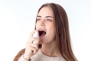 junges Mädchen, das Halsschmerzenspray spritzt, ist auf einem weißen Hintergrund isoliert foto