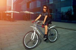 süße brünette sportfrau mit sonnenbrille auf einem fahrrad foto