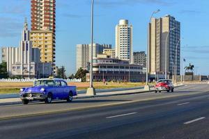 havanna, kuba - 15. jan 2017 - klassisches auto, das entlang des malecon mit der casa de las americas im hintergrund in havanna, kuba fährt. foto