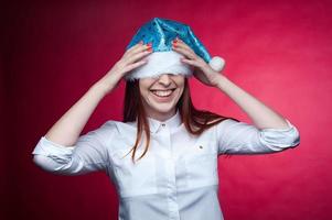 mädchen, das im studio auf einem rosa hintergrund, in einer weihnachtsmütze aufwirft foto